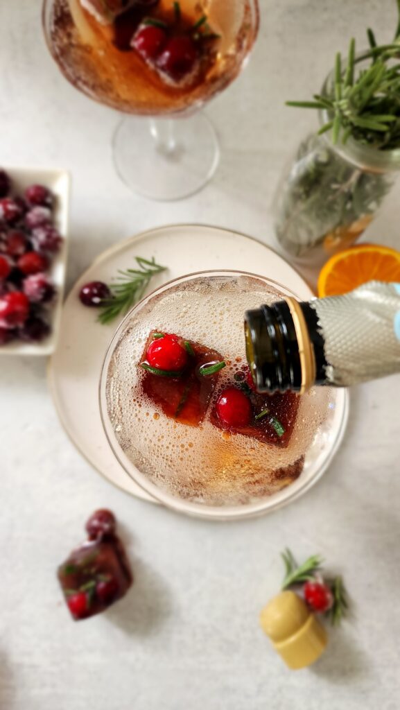 Top Shot pouring champagne over a pomegranate ice cube for a pomegranate mimosa