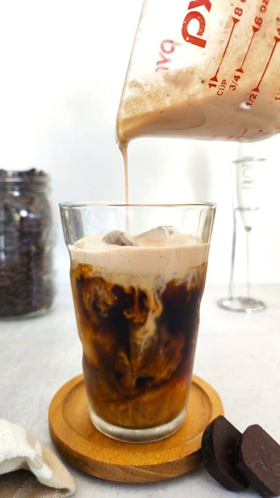 Pouring chocolate cream into a glass of cold brew coffee