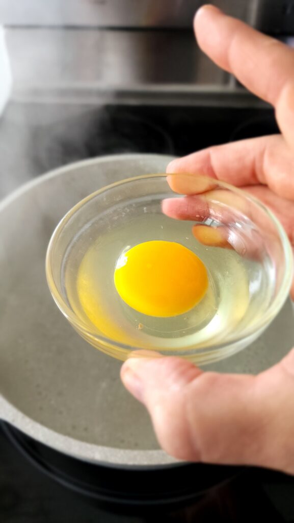 Egg in a small bowl being dropped into the water