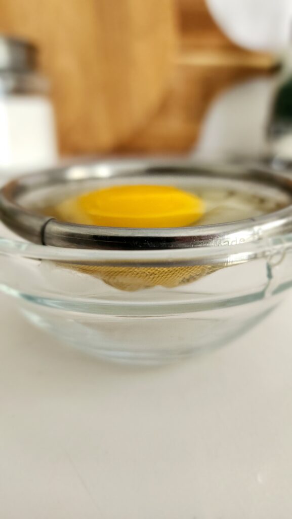 Egg in a fine mesh sieve over a bowl removing excess egg white