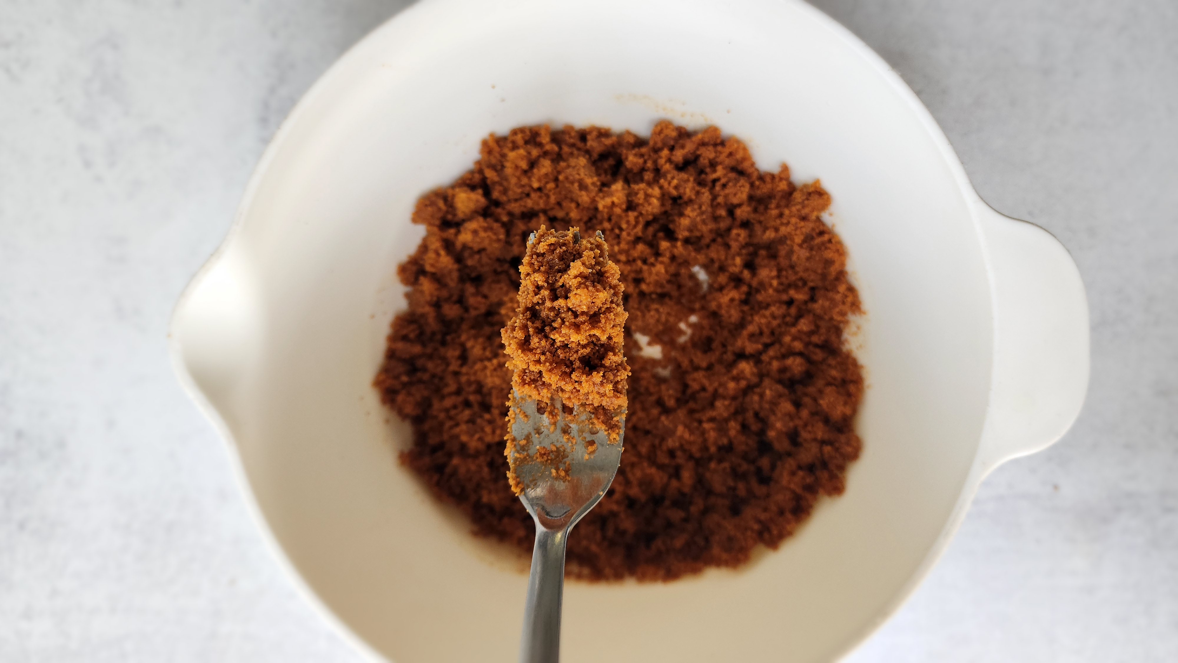 bowl of cookie crumbs mixing the melted butter in with a fork