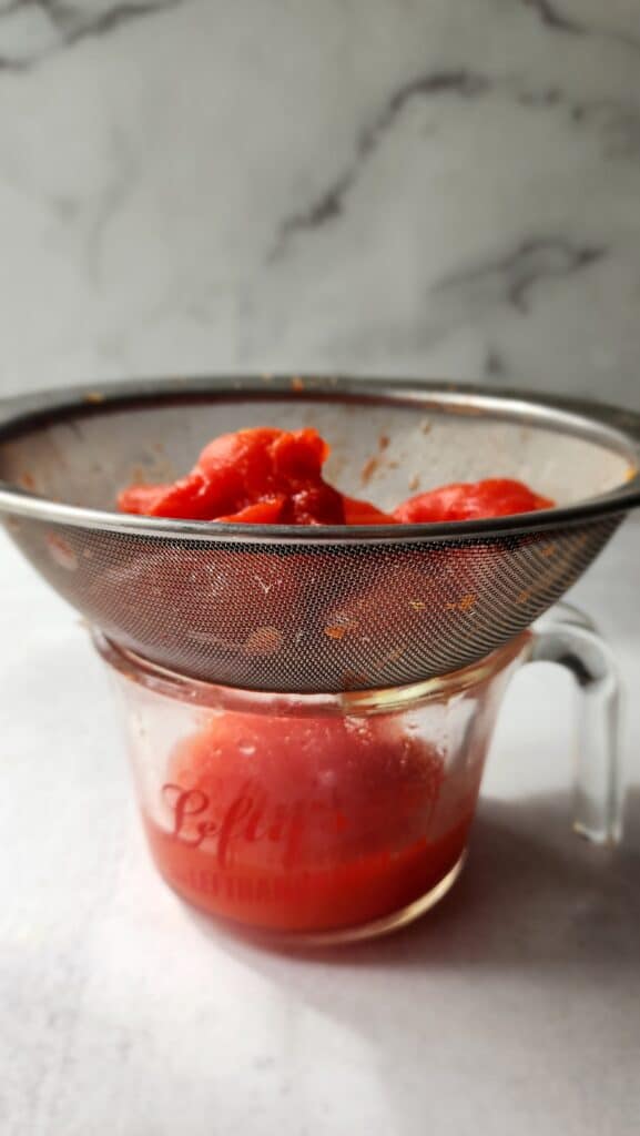canned tomatoes sitting in a colander over a pyrex measuring cup to drain the tomatoes