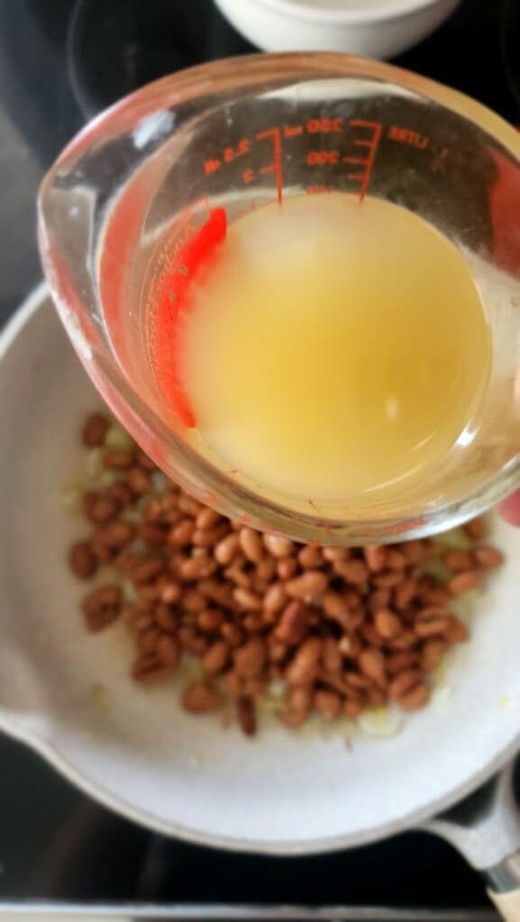 adding in broth to make homemade refried beans