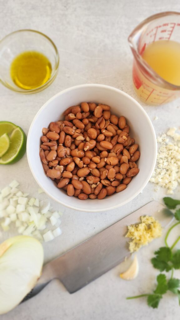 ingredients to make homemade refried beans: pinto beans, garlic, onion, lime juice, broth, cotija cheese, cilantro