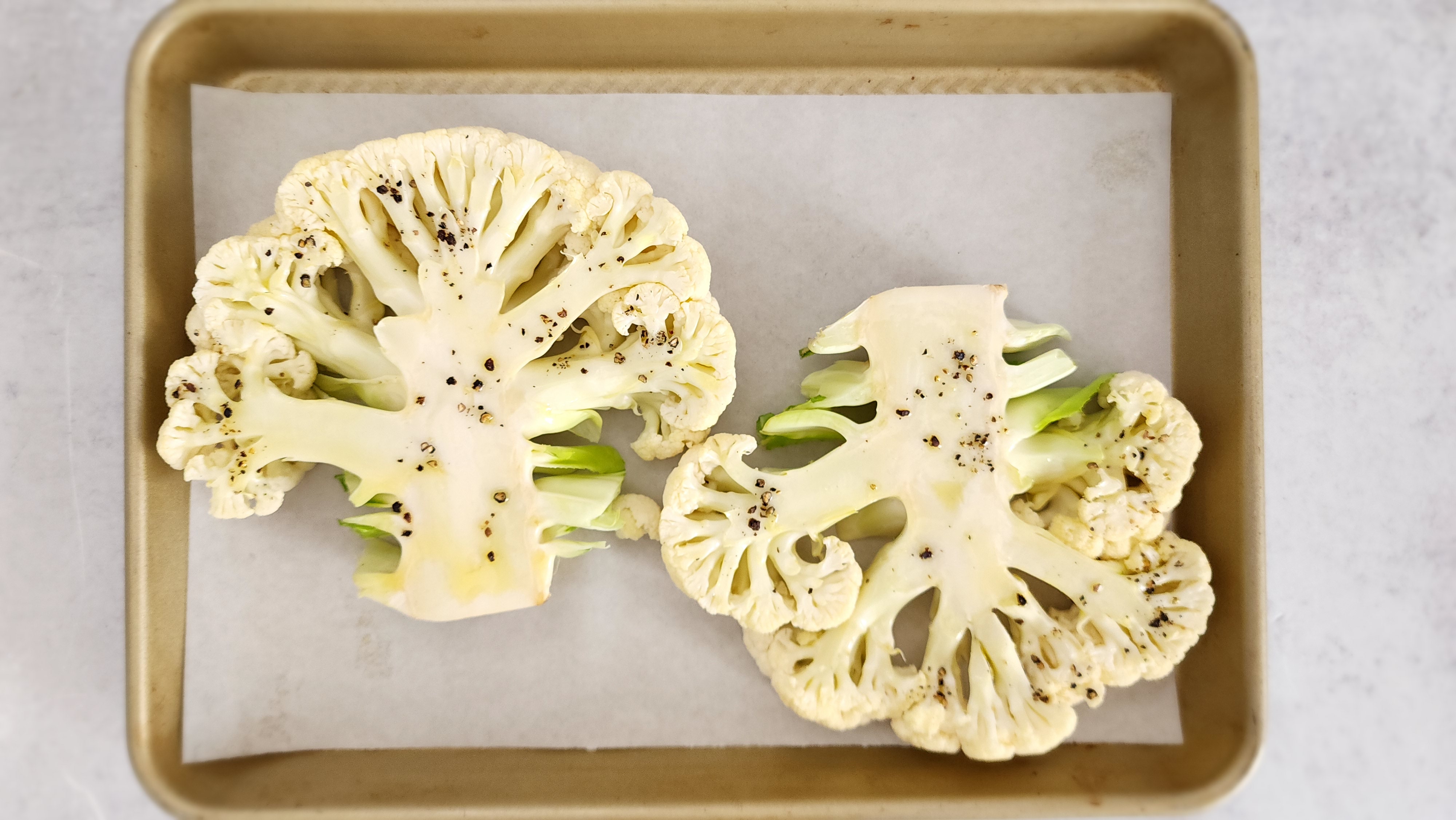 two cauliflower slices ready to be roasted, coated with olive oil