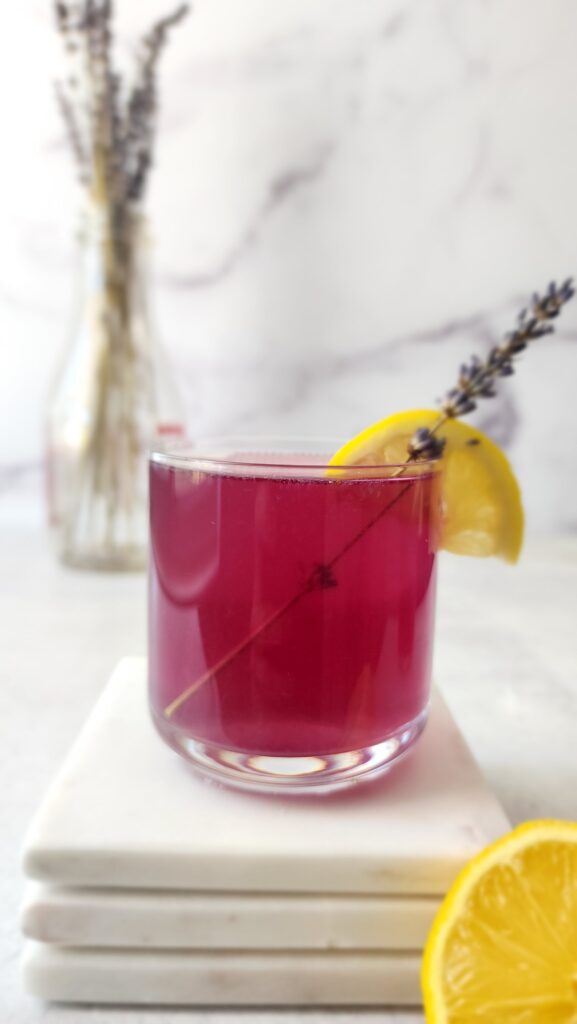 glass of butterfly pea flower cocktail with a sprig of lavender