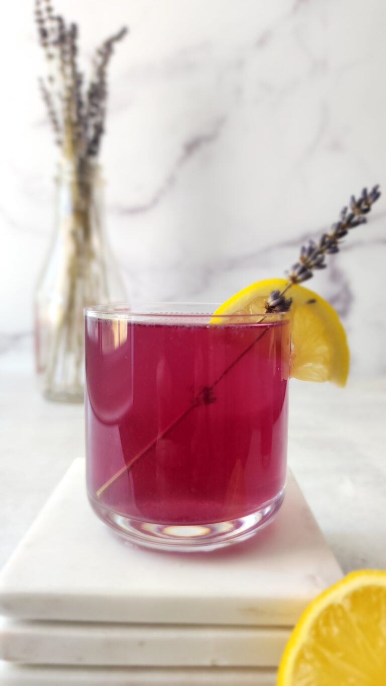 side shot of the butterfly pea flower cocktail with a garnish of lavender and a lemon slice