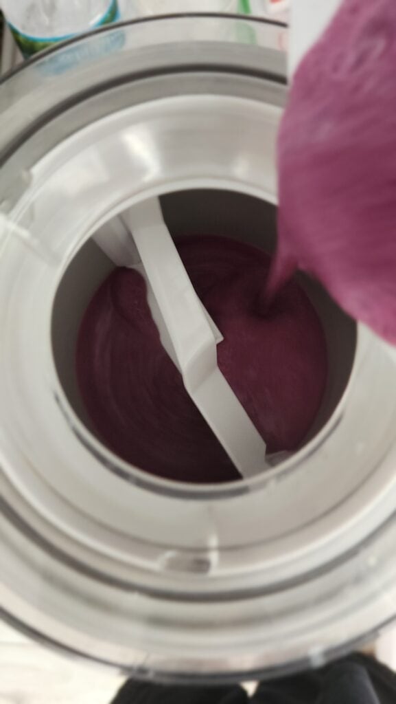 adding blueberry mixture to the ice cream maker to make frozen blueberry yogurt