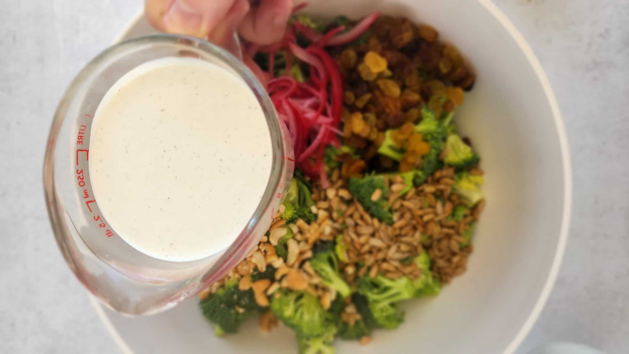 the Gree yogurt/mayonnaise dressing in a measuring cup ready to pour over the bowl of broccoli salad