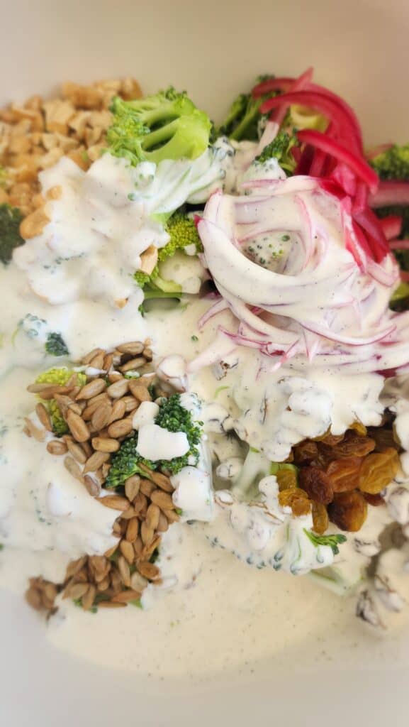 mayonnaise/Greek Yogurt dressing drizzled on top of all the ingredients for broccoli salad