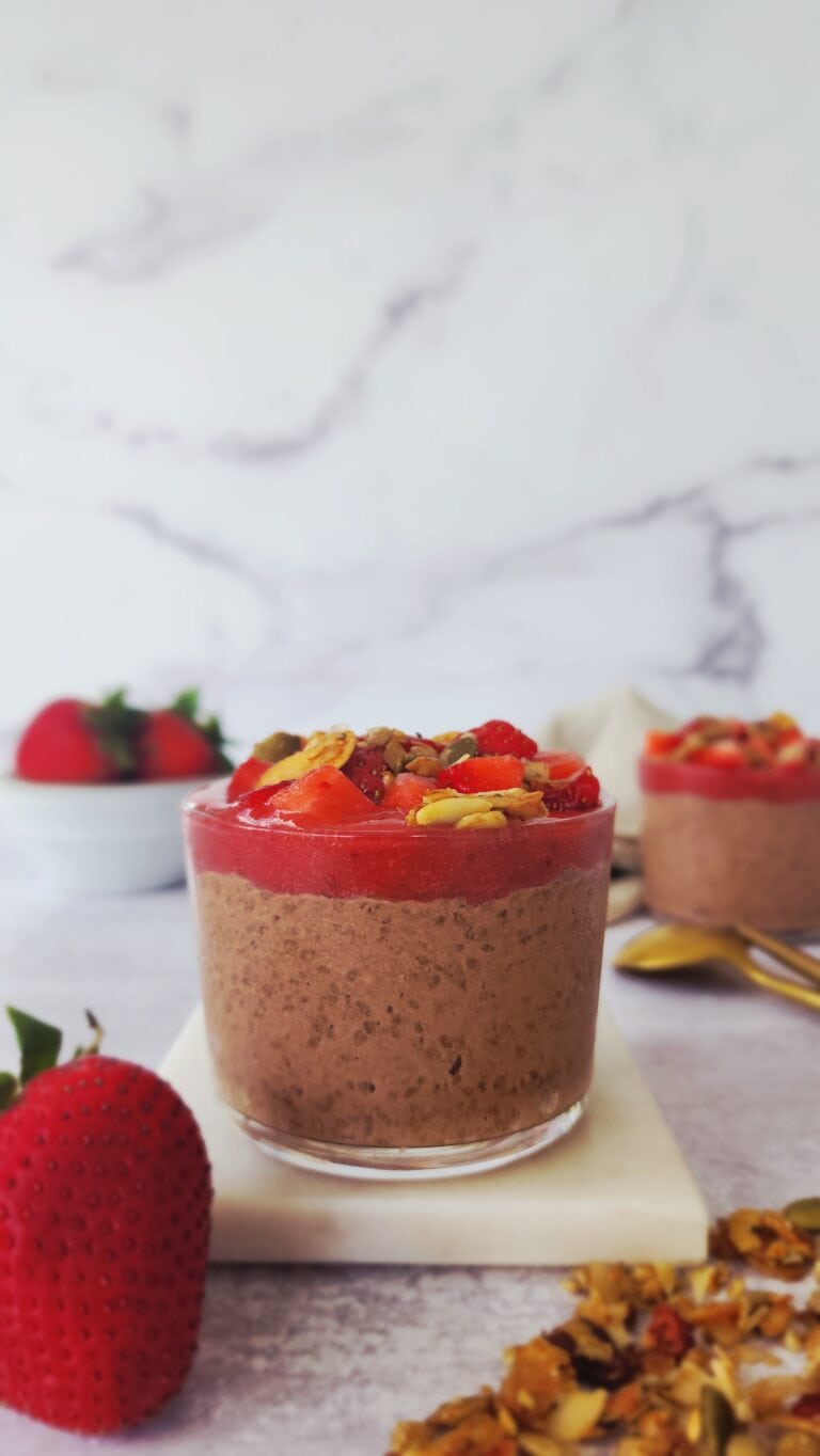 glass of chocolate chia seed pudding with easy strawberry sauce and homemade granola on top