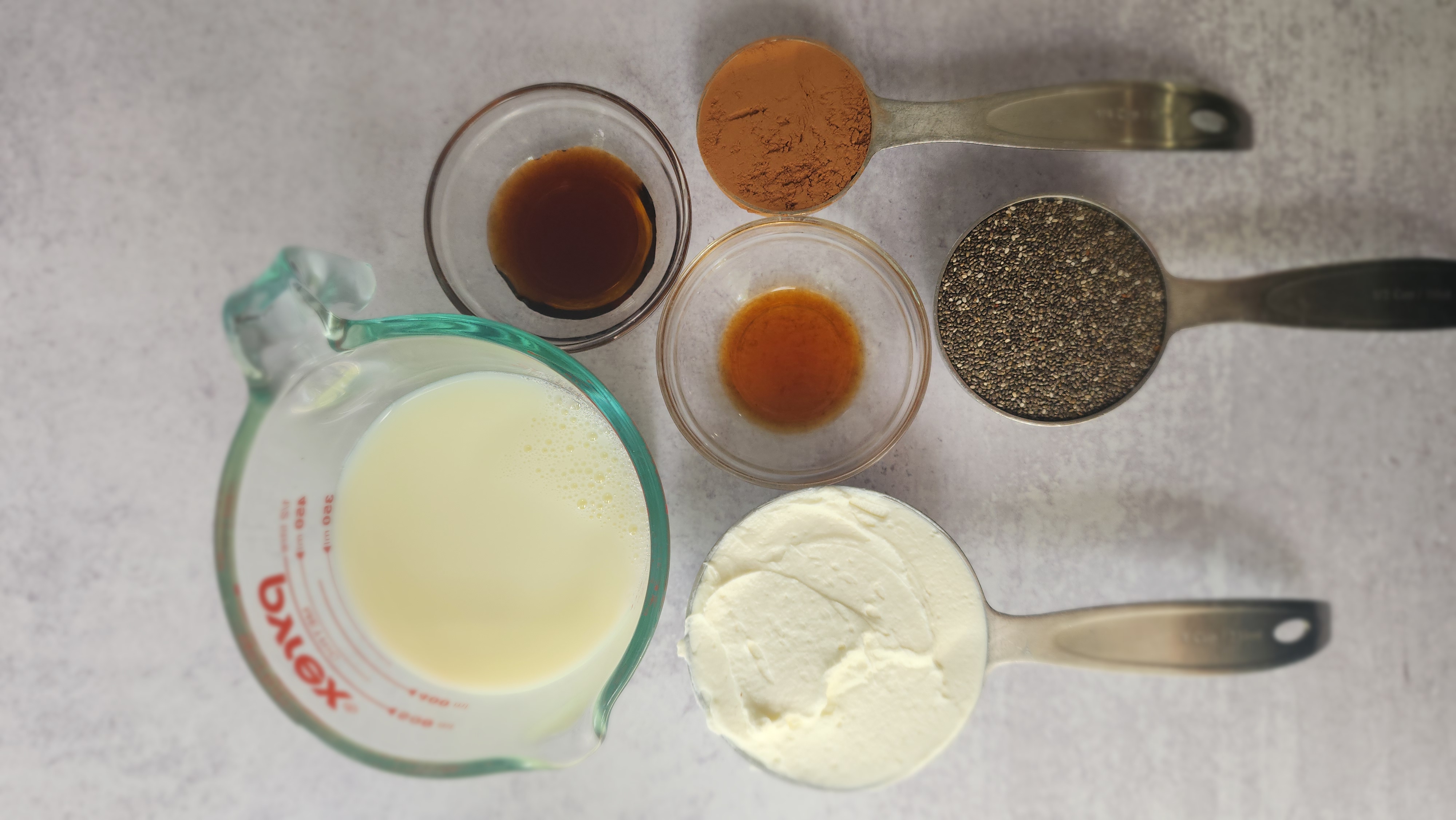 all the ingredients laid out to make chocolate chia seed pudding: milk, chia seeds, Greek yogurt, maple syrup, vanilla, cocoa powder