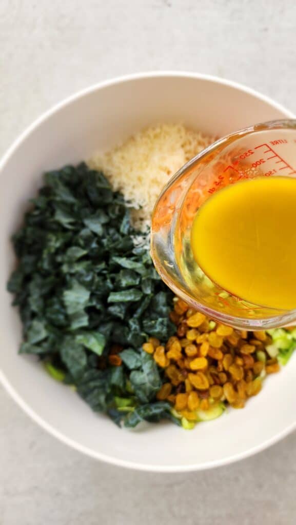 all the ingredients in a bowl for kale brussels salad with lemon vinaigrette dressing about to be drizzled on top