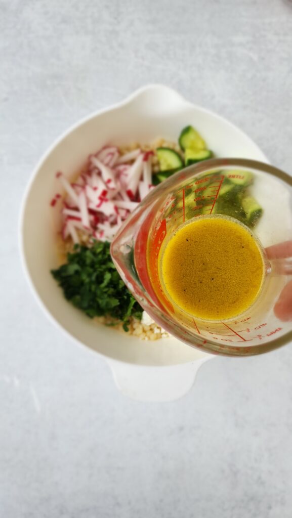 adding in the lemon vinaigrette above the bowl of lemon couscous salad