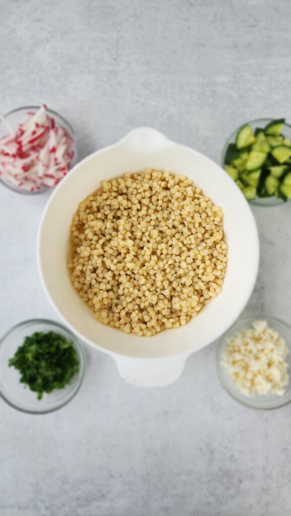 bowl with couscous, and little bowls with radish, parsley, cucumber, and feta cheese for lemon couscous salad