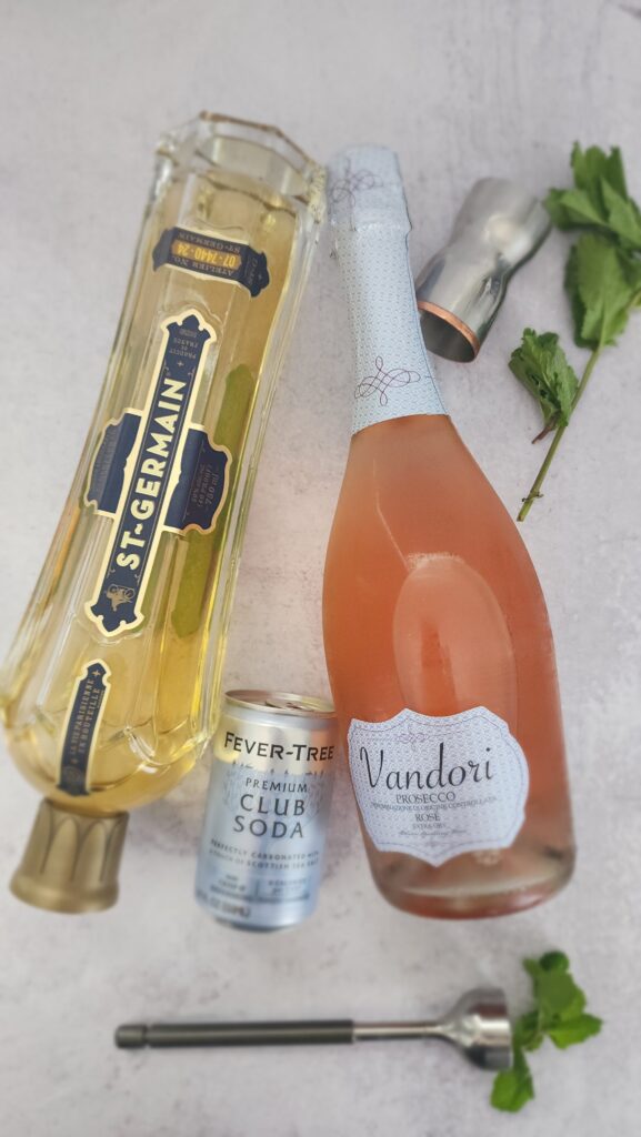 all the ingredients to make a Rose Hugo Spritz - Rose Prosecco, Elderflower Liquor, club soda, mint