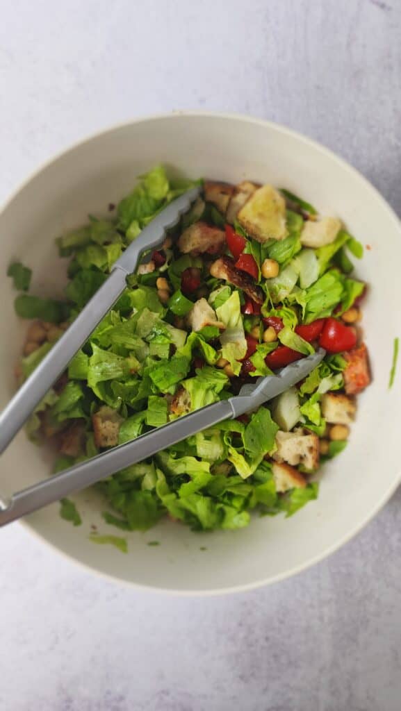tongs tossing all the ingredients in a bowl together for panzanella salad