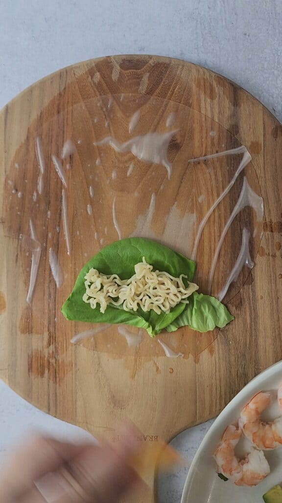 cutting board with soaked rice paper with lettuce and noodles getting ready to make the layers for an easy shrimp spring roll