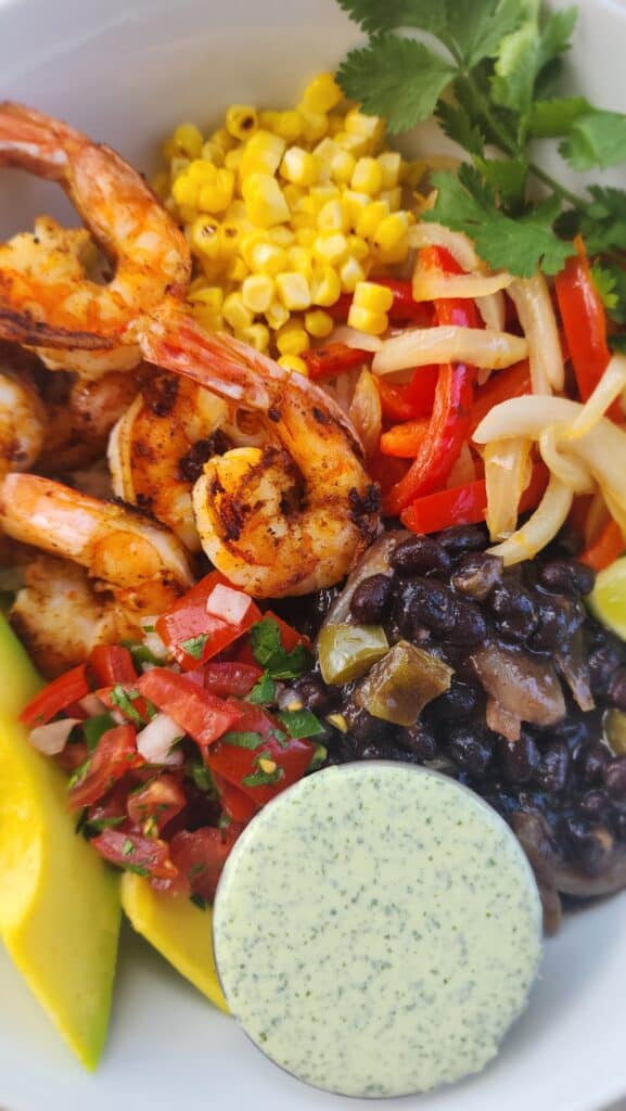 bowl of blackened shrimp with black beans, sauteed peppers, grilled corn, salsa, avocado, and cilantro jalapeno sauce