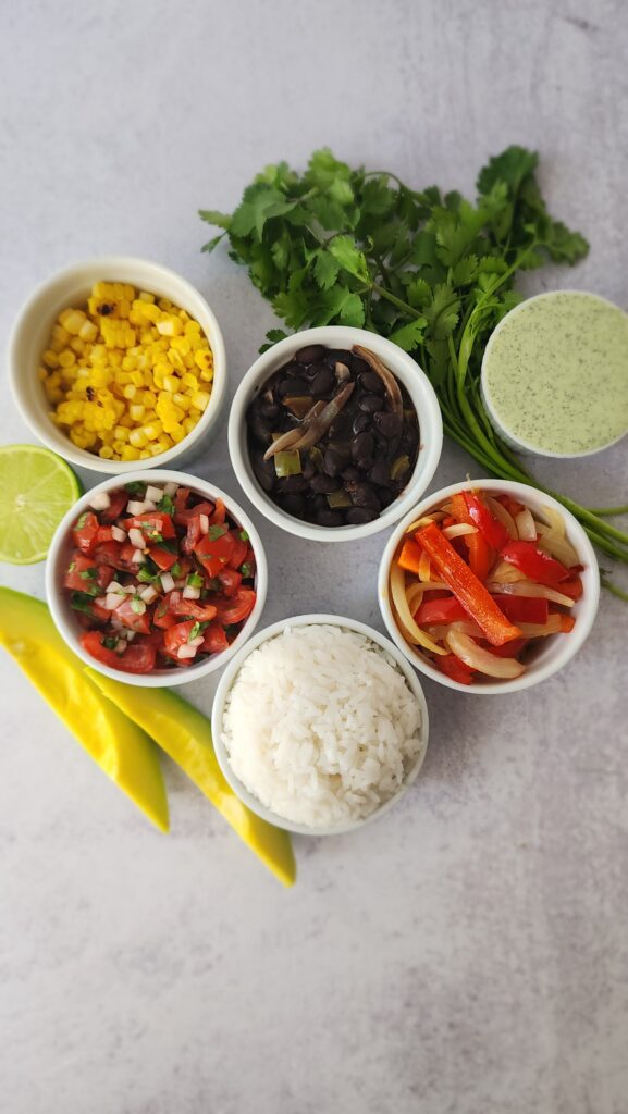 ingredients to make the Chipotle Burrito Bowls: black beans, white rice, sauteed peppers and onions, avocado, pico de gallo, charred corn, and cilantro jalapeno sauce