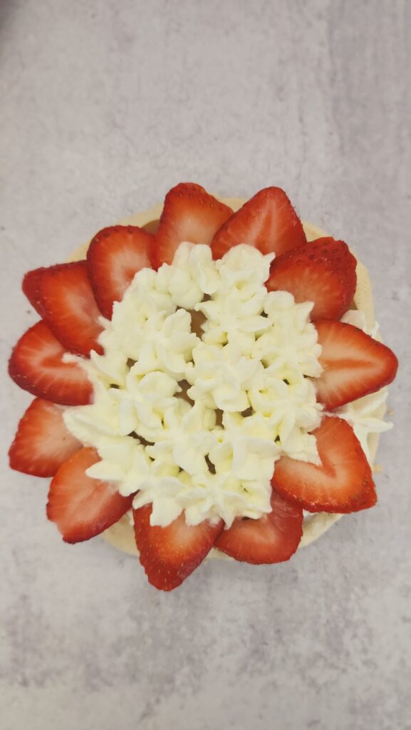 the makings of a strawberry pavlova and the pavlova is on the bottom with then the dulce de leche, next the whipped cream, and now the strawberries are being assembled