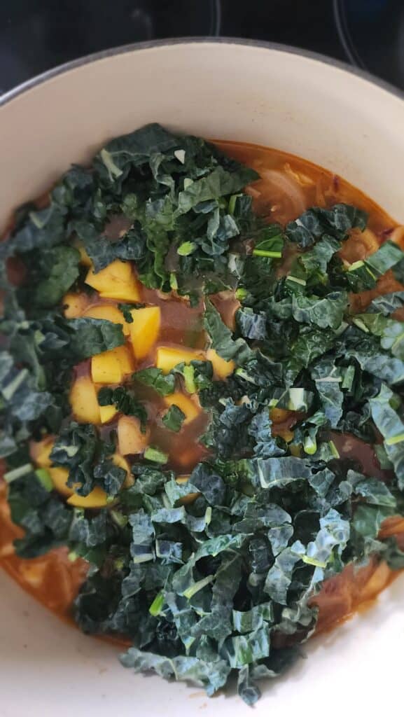 adding kale and potatoes to simmered veggies for Easy Ribollita Soup