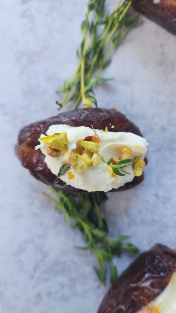 up close of one single goat cheese stuffed date with thyme & pistachios
