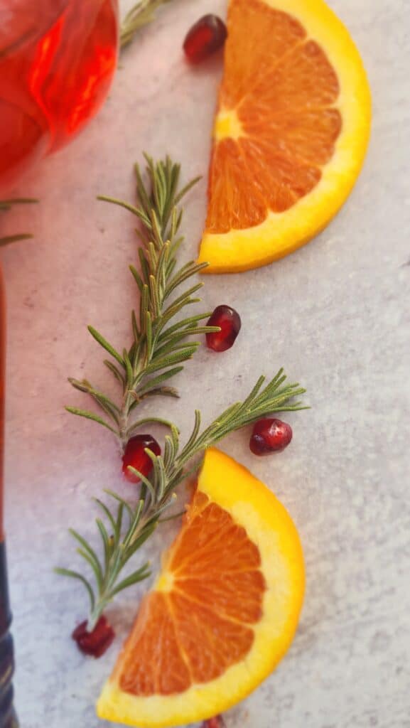 garnish of orange slices, pomegranate arils, and a rosemary sprig for the Holiday Aperol Spritz