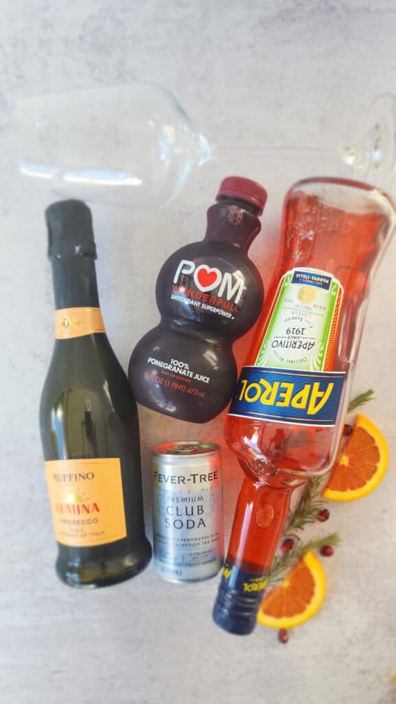 all the ingredients to make a Holiday Aperol Spritz: Aperol, Pomegranate juice, Prosecco, and club soda