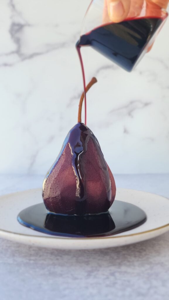 red wine poached pears with the syrup drizzled on top of a pear on a dessert plate