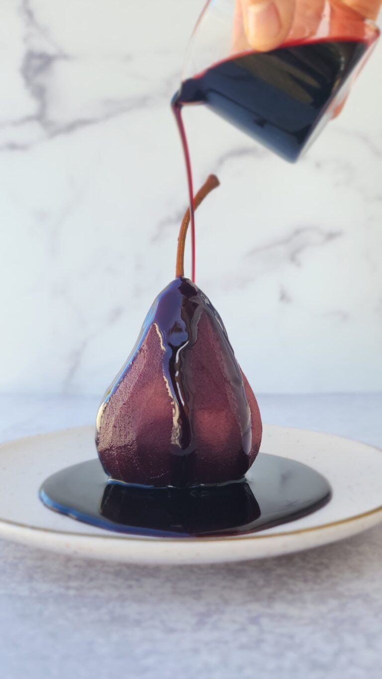 red wine poached pears with the syrup drizzled on top of a pear on a dessert plate