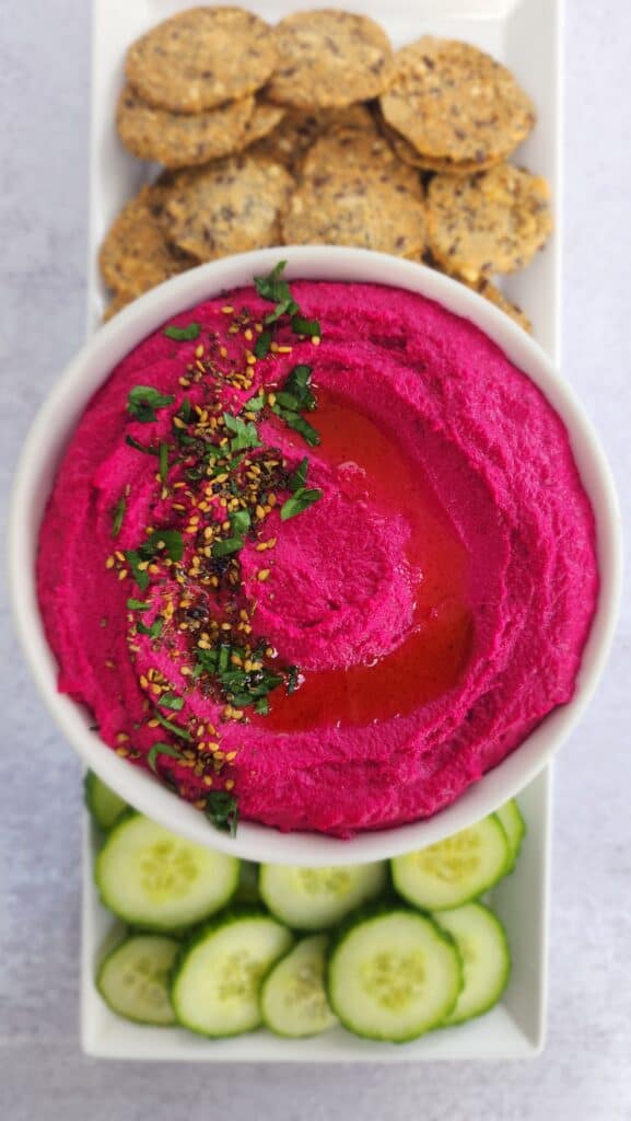 Roasted Beet Hummus in a bowl served with crackers and cucumber