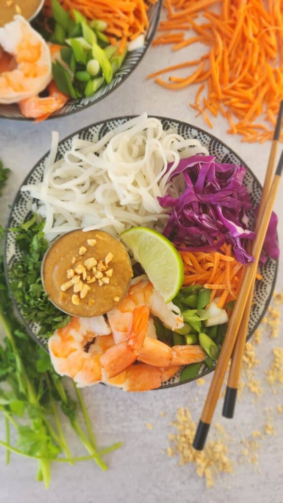 bowl of cold peanut soba noodles with shredded carrots, shredded cabbage, sliced green onions, cilantro, and peanut sauce