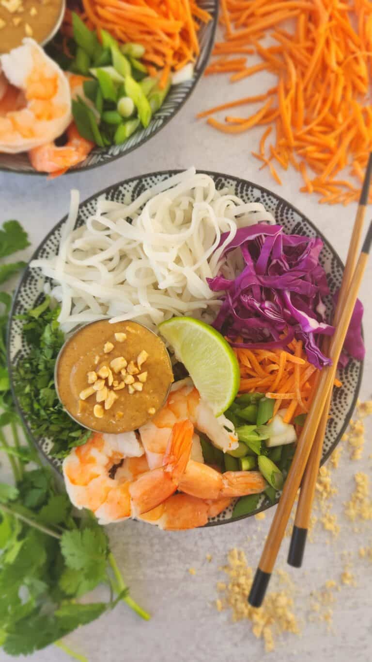 bowl of cold peanut soba noodles with shredded carrots, shredded cabbage, sliced green onions, cilantro, and peanut sauce