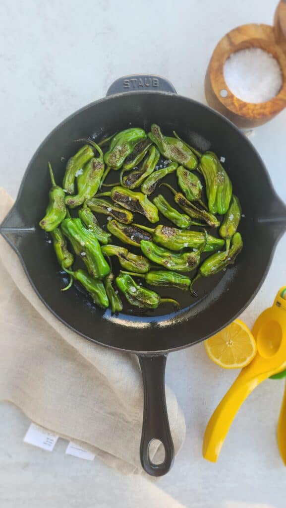 cast-iron skillet filled with grilled shishito peppers