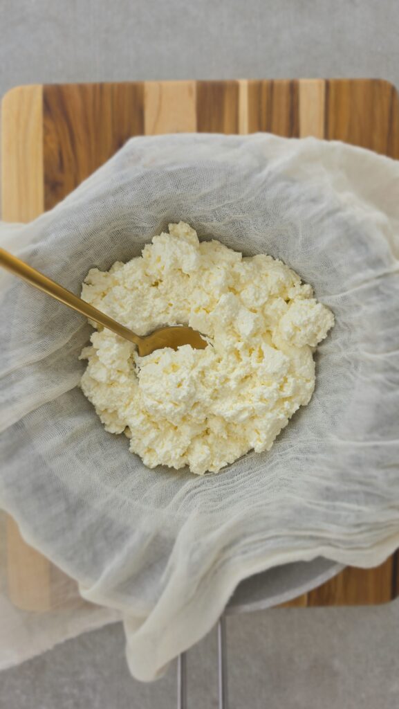 strained homemade ricotta in a cheesecloth over a colander