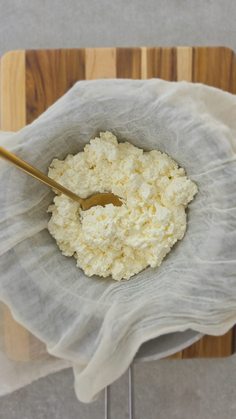 strained homemade ricotta in a cheesecloth over a colander