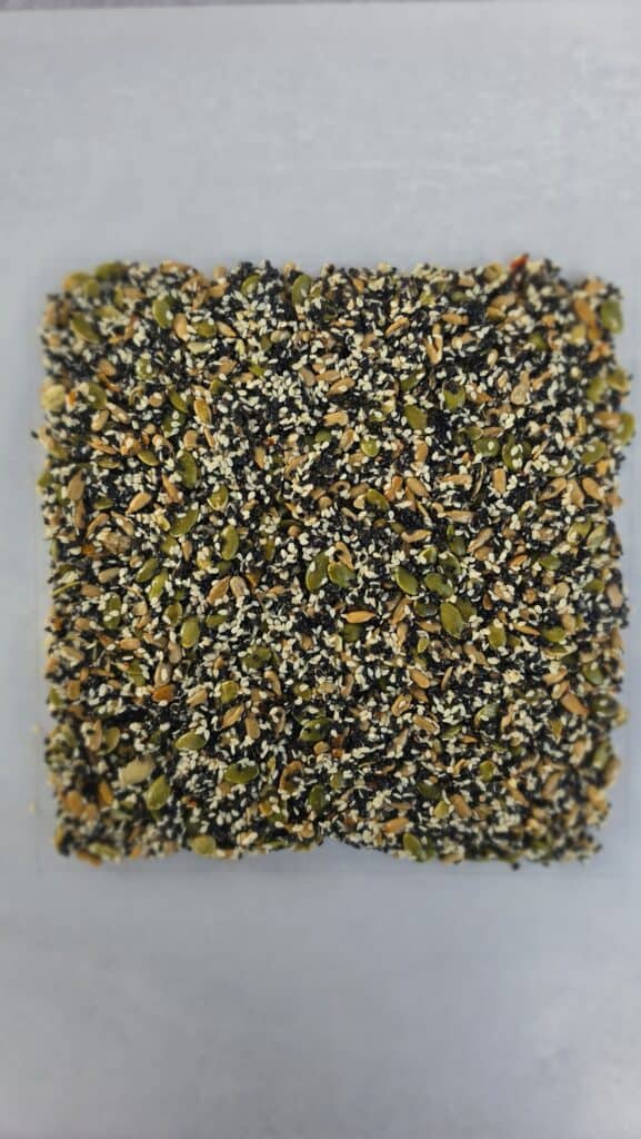 8x8 square of seed brittle on parchment paper ready to be baked