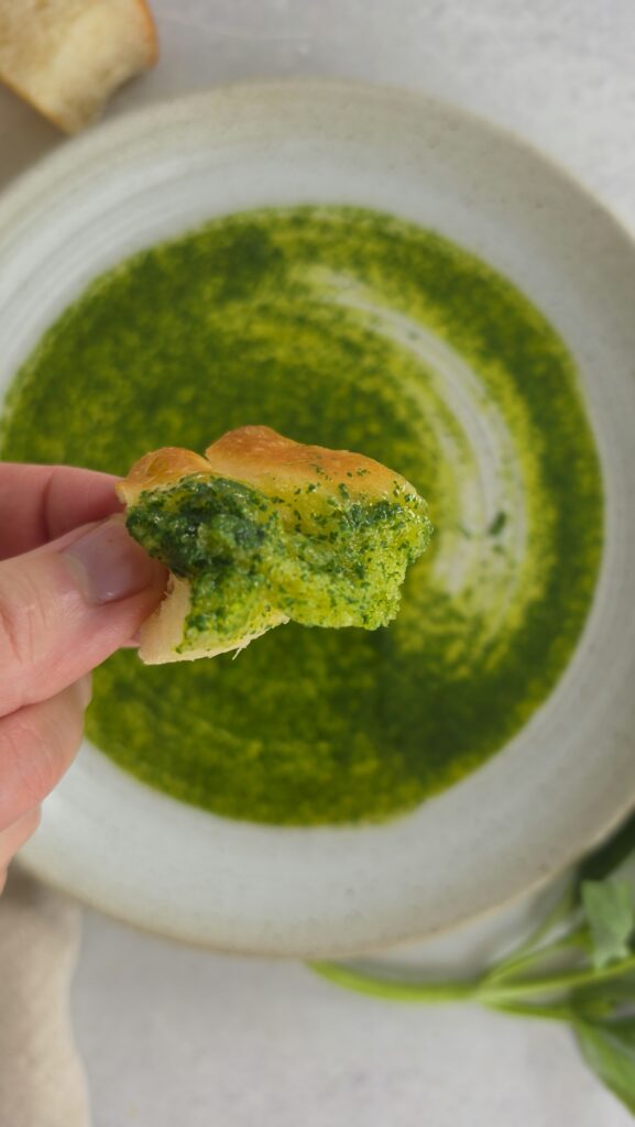 plate of basil oil with a piece of bread being dredged through the basil oil