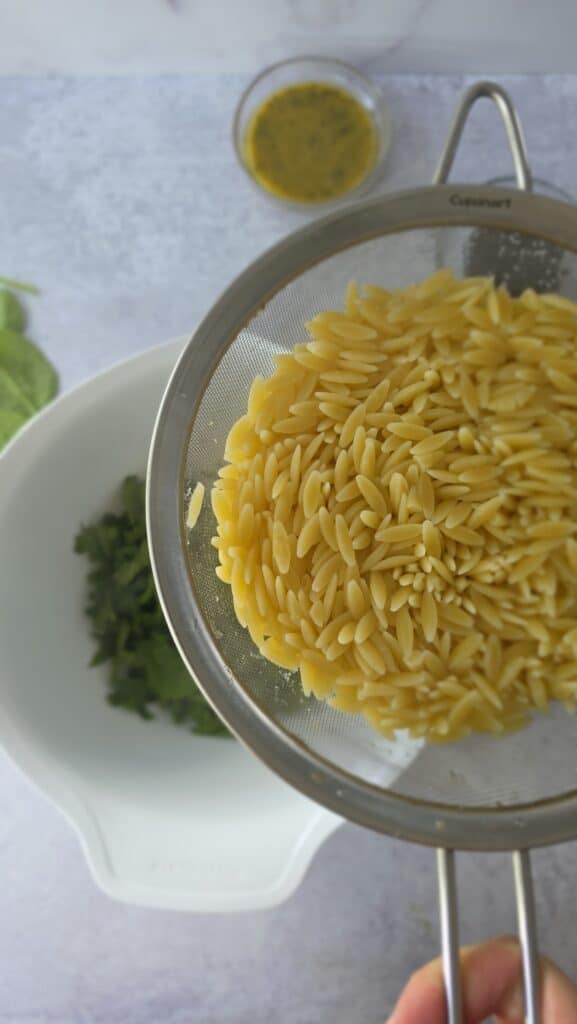cooked spinach in a bowl being added to the julienned spinach to wilt the spinach for orzo salad
