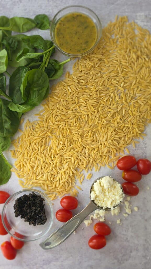 ingredients for orzo salad with orzo, spinach, tomatoes, feta cheese, black olive, and Italian salad dressing