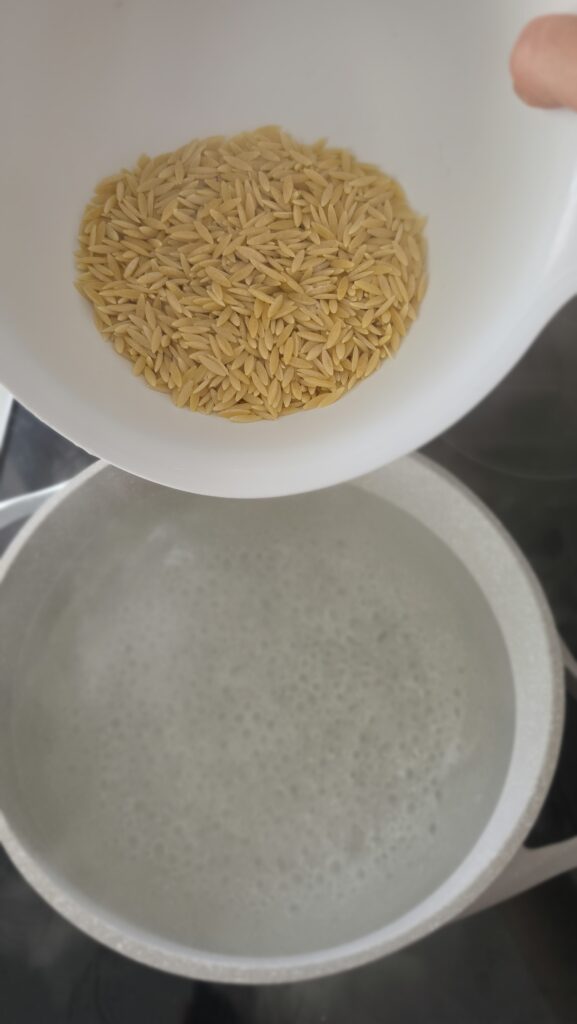orzo being added to boiling water for orzo salad