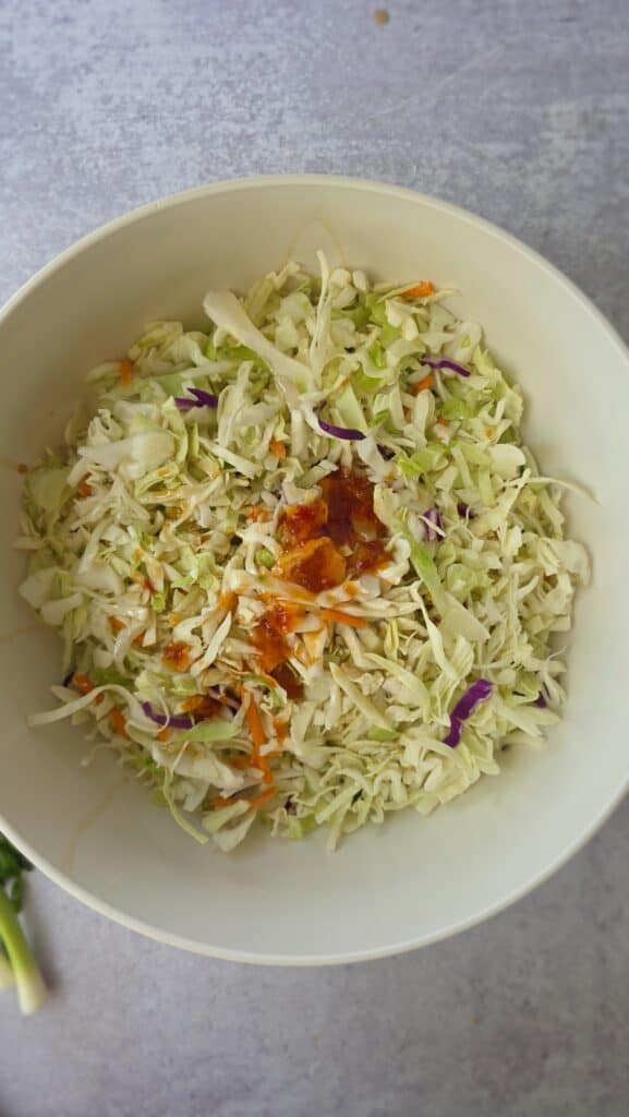 adding the dressing to the cabbage mix for a sesame ginger slaw