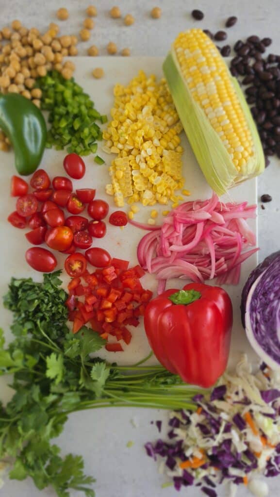 ingredients for dense bean salad: chickpeas, black beans, tomatoes, pickled red onion, corn, cabbage, cilantro jalapeno dressing