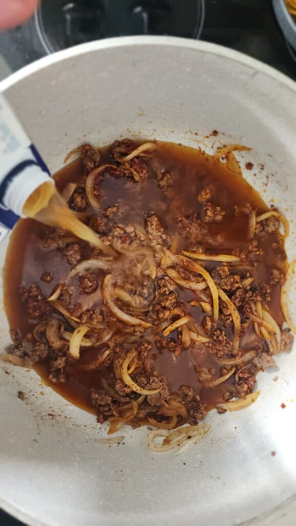 adding beef broth into the cooked ground beef