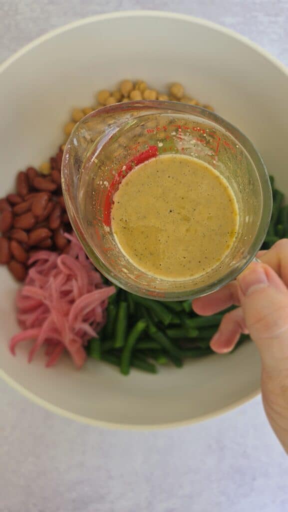 adding the red wine vinaigrette to the easy three-bean salad